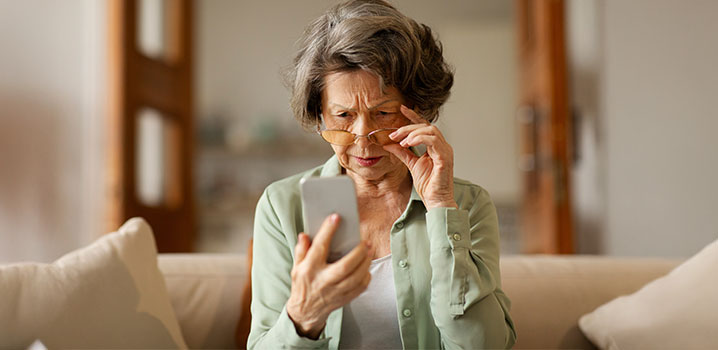 Alte Frau mit Brille sitzt auf Sofa und hält Smartphone in der Hand